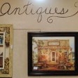 The word antiques is painted on the room wall above a photo of a general store and a gold framed mirror.